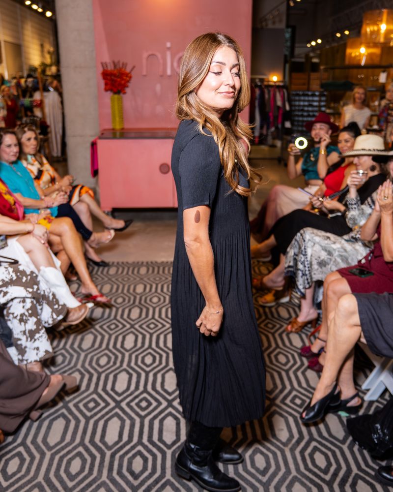model in a black dress, heart necklace and cowboy boots walking down a runway