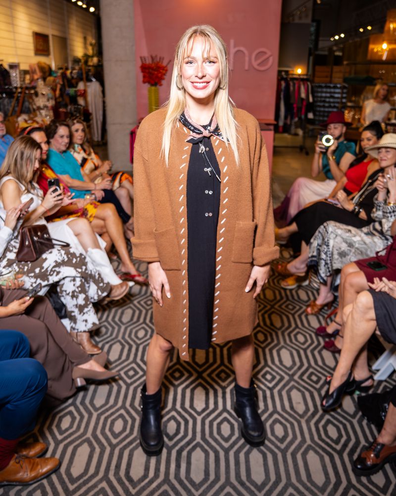 model wearing black twinbutton dress with brown cardigan, bandana and boots on a runway
