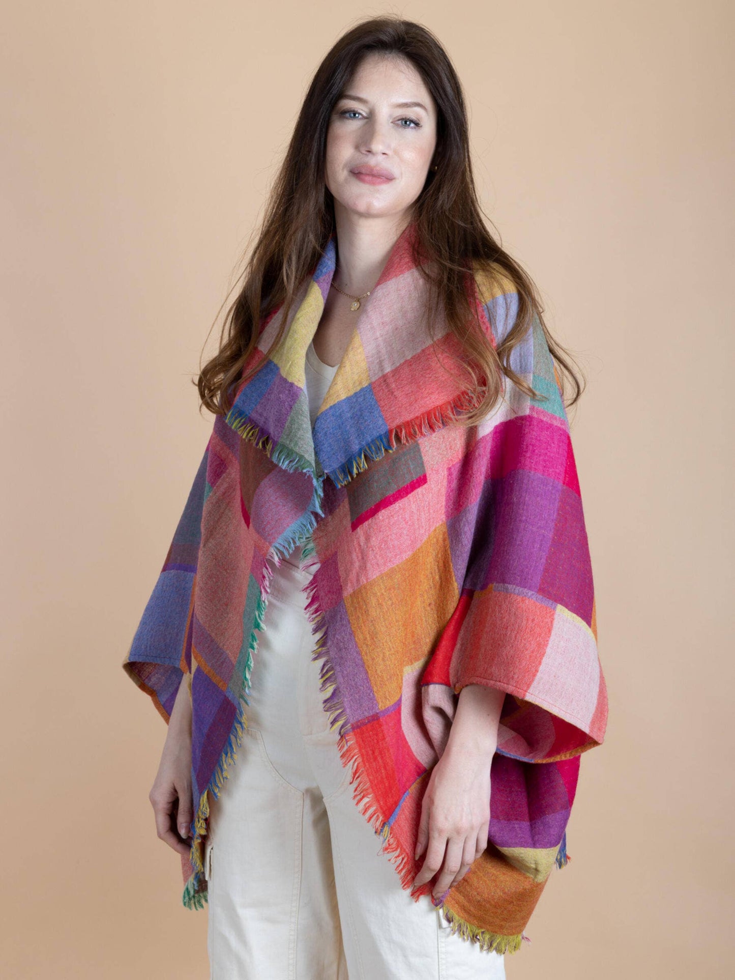 model is wearing an all white outfit with rainbow color-blocked wool poncho on top