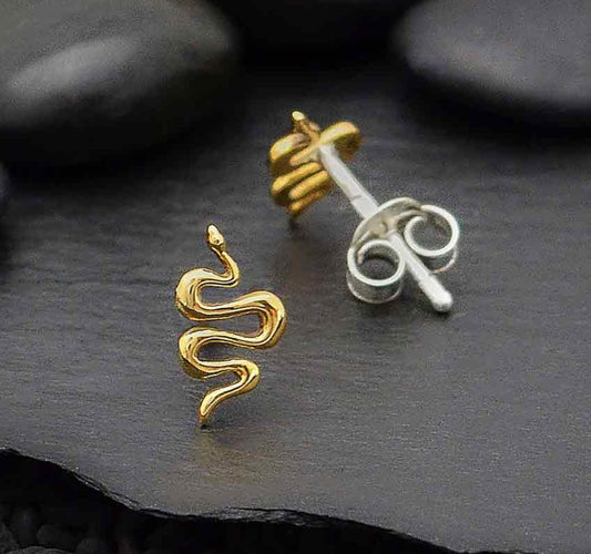 shiny bronze earrings in shape of a windy snake. against a dark slate background with pebbles 