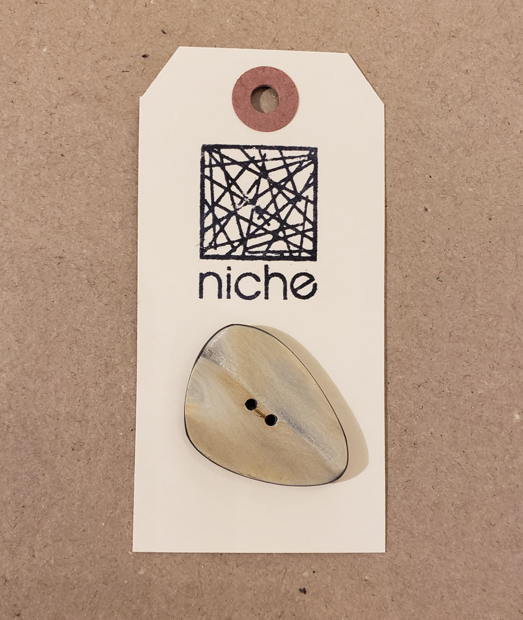 asymmetrical tan button on a Niche card