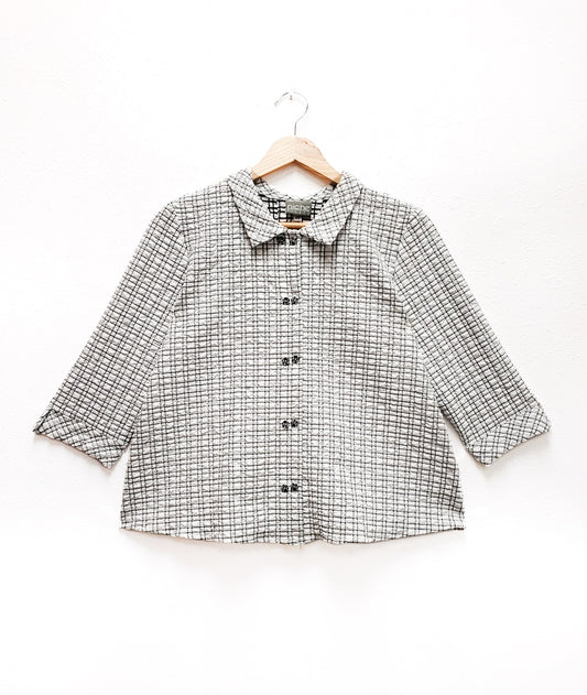 white and black grid print textured button up blouse on a hanger and white background
