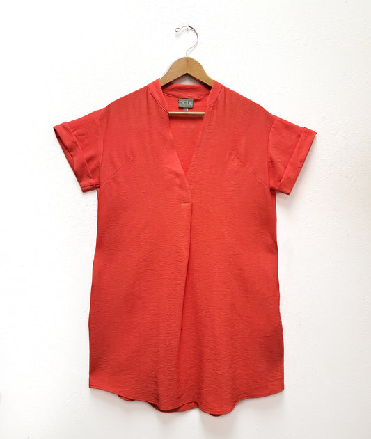 coral color boxy dress with a v neck on a wooden hanger on a white wall