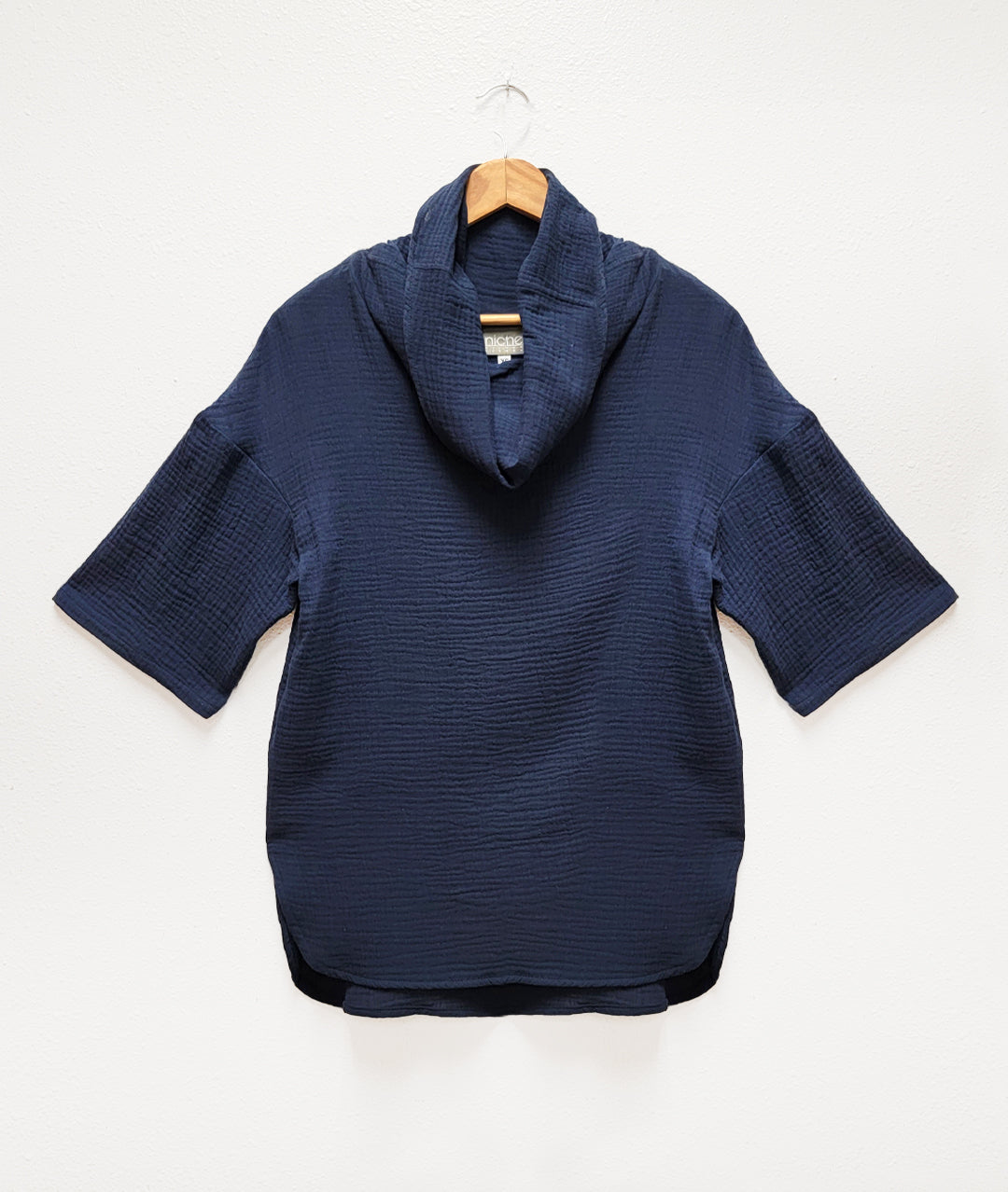 navy blue boxy top with short sleeves, a rounded hem and a cowl neck, on a wooden hanger