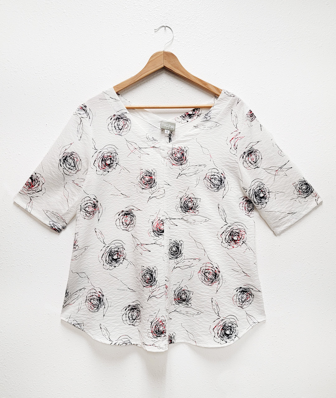 white blouse with a red and black rose print. top has elbow length sleeves and a v shape neckline in the front and back