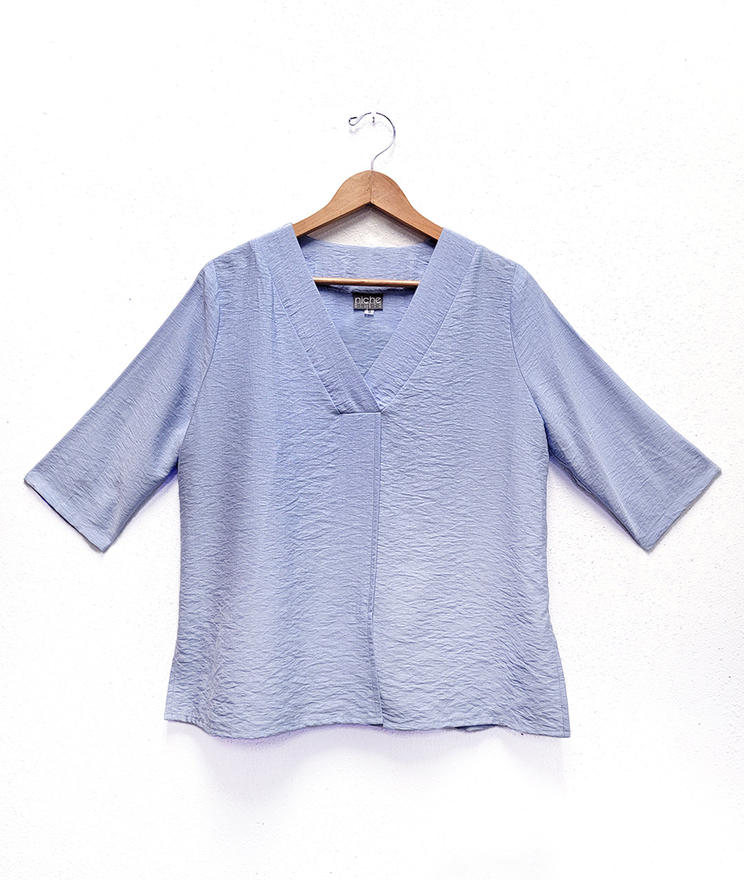 light blue top with a vneck and 3/4 sleeves. top has a center front seam and splits on either side.