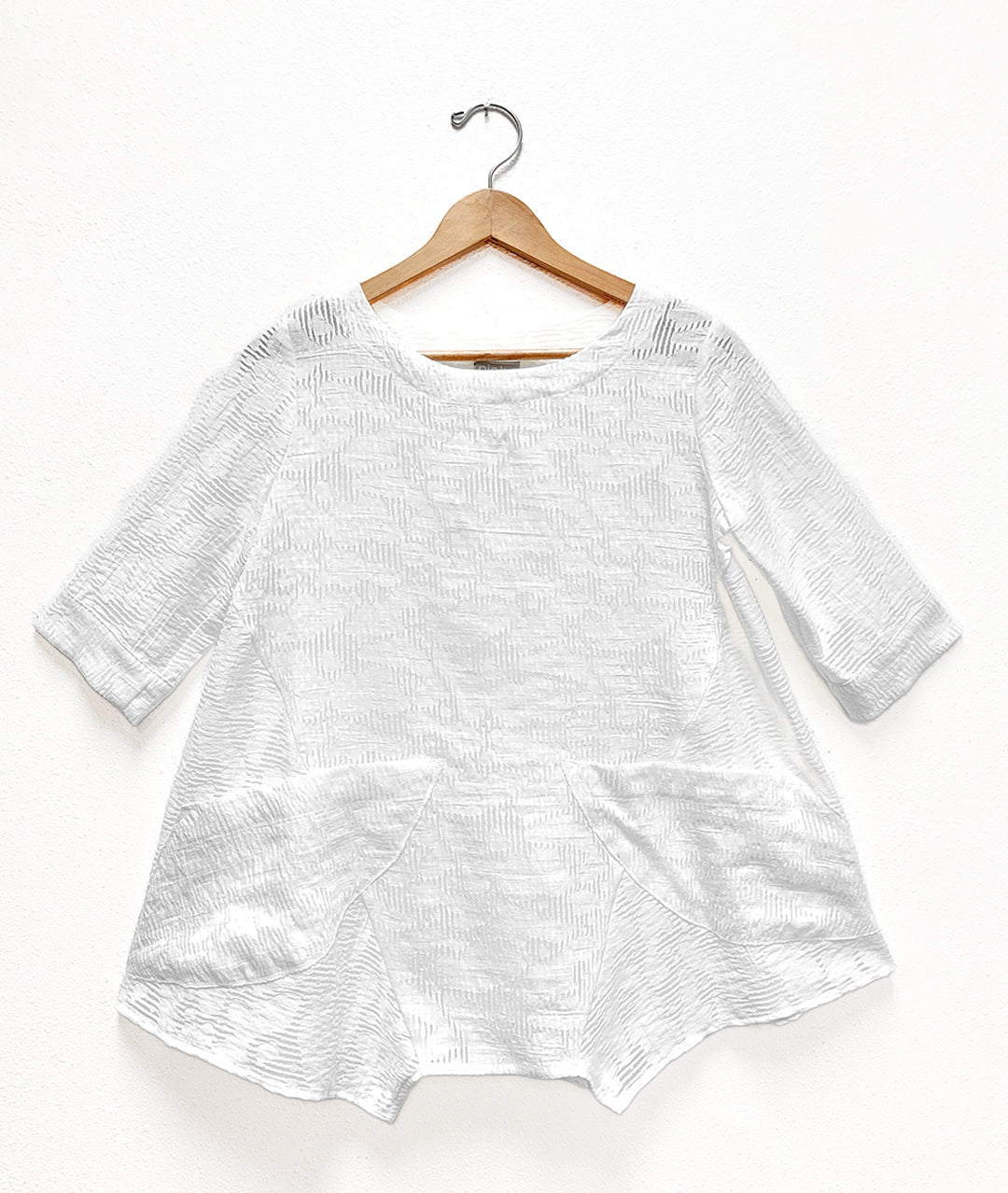 a white pullover top with a round neckline, 3/4 sleeves, half moon hip pockets, on a wooden hanger