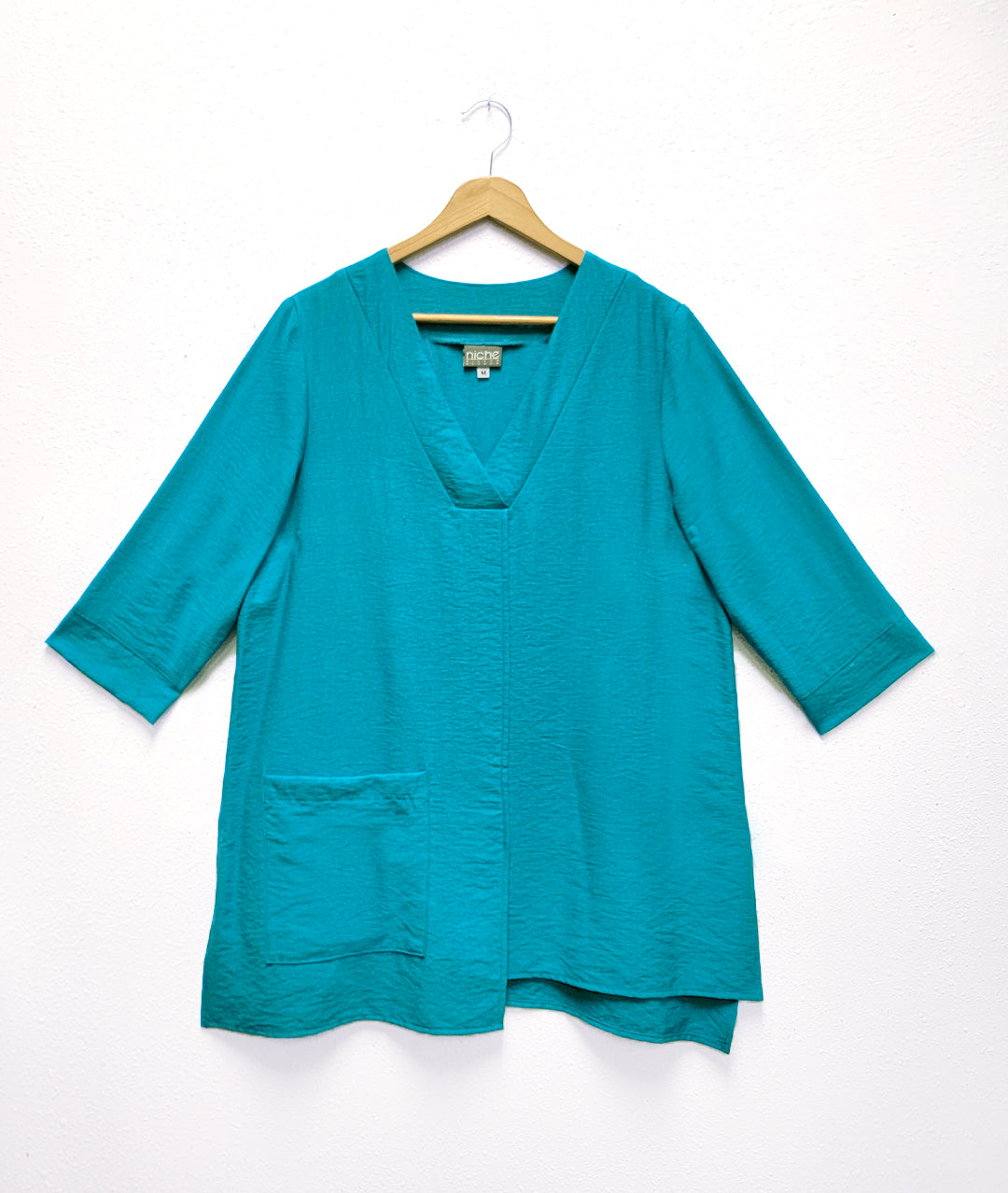 turquoise pull over top with 3/4 sleeves, a vneck, asymmetrical hem line and single squared hip pocket