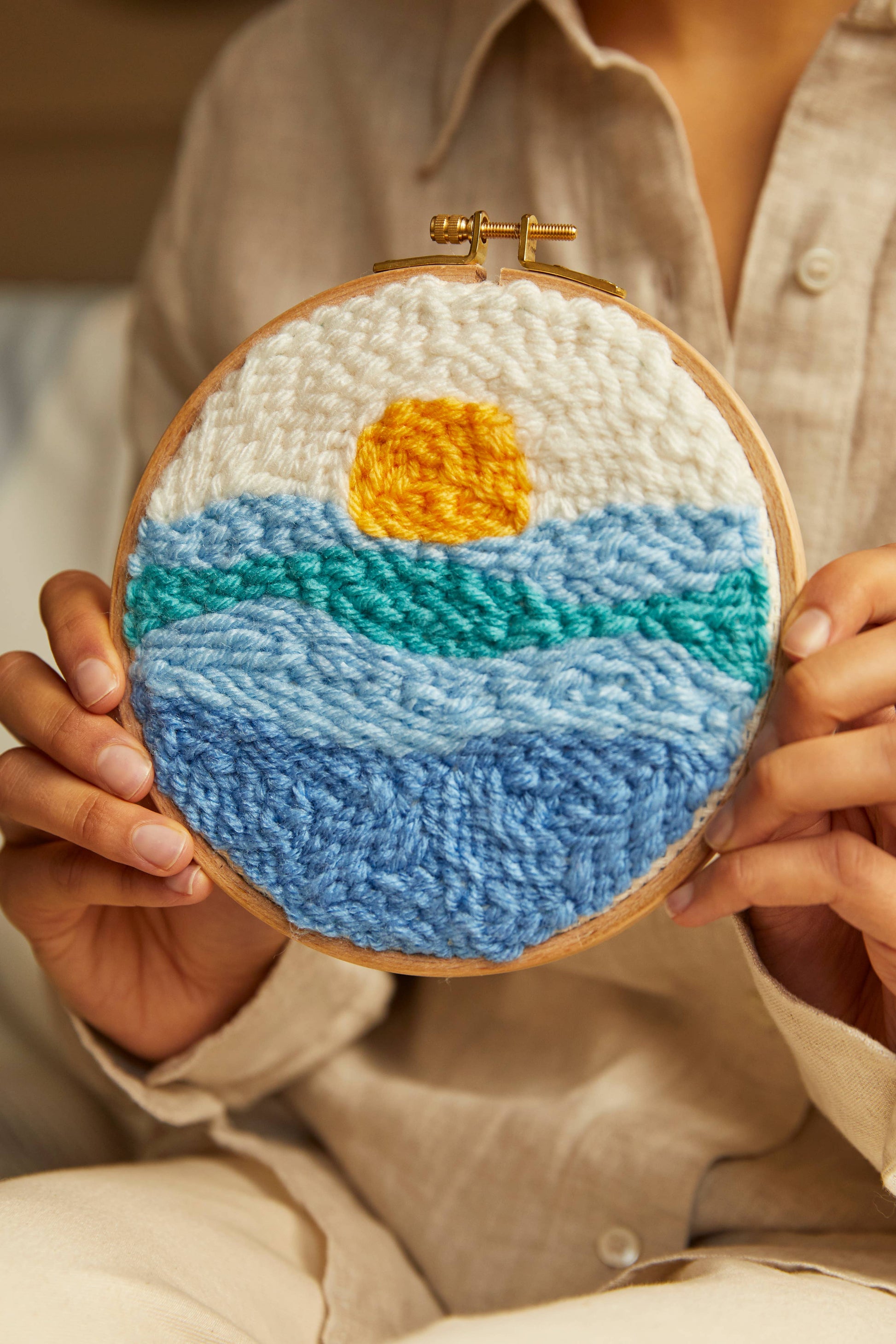 Embroidery hoop with embroidered design of sunset and water