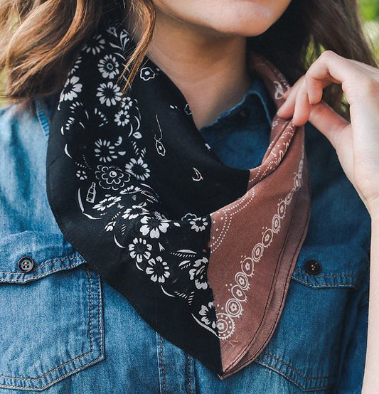 Pictured is a model wearing a denim buttoned up shirt and a bandana around her neck. The bandana is navy colored on one side and rust on the other. 