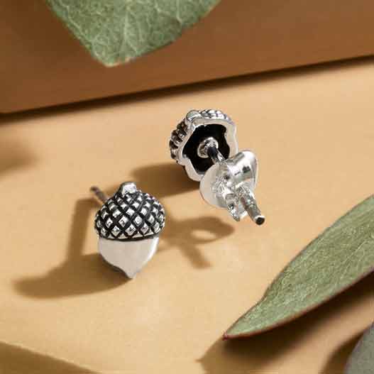 Petite post earrings in the shape of acorns on a clay background