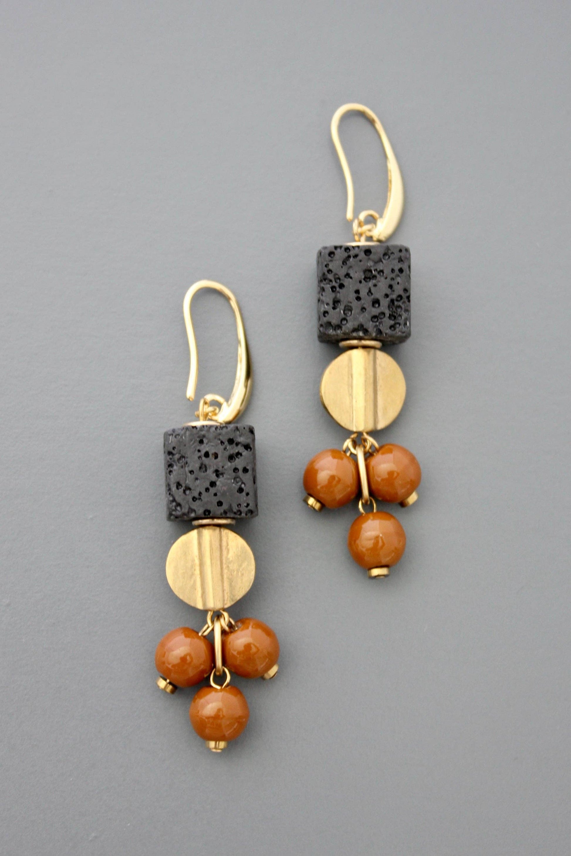 Gold plated brass hooks with lava and glass beads against a grey background