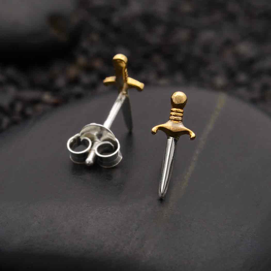 This image features a pair of intricately designed dagger post earrings, crafted from sterling silver. The earrings are designed to resemble miniature dagger handles, complete with detailed grips and pointed tips, showcasing a high level of detail and craftsmanship.