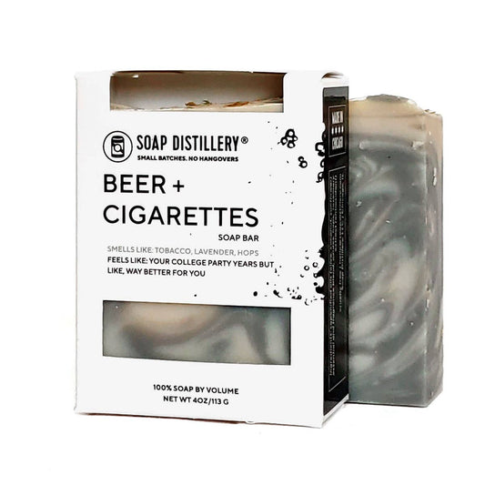 Photo of grey and cream marbeled bar of soap next to a packaged bar of soap in a black and white box with a label that says "Beer + Cigarettes" with a description.