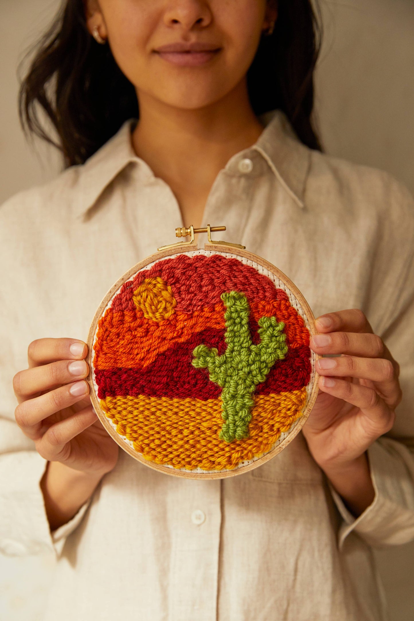 Girl holding embroidery hoop with embroidered cactus and sunset design in orange, red, yellow, and green