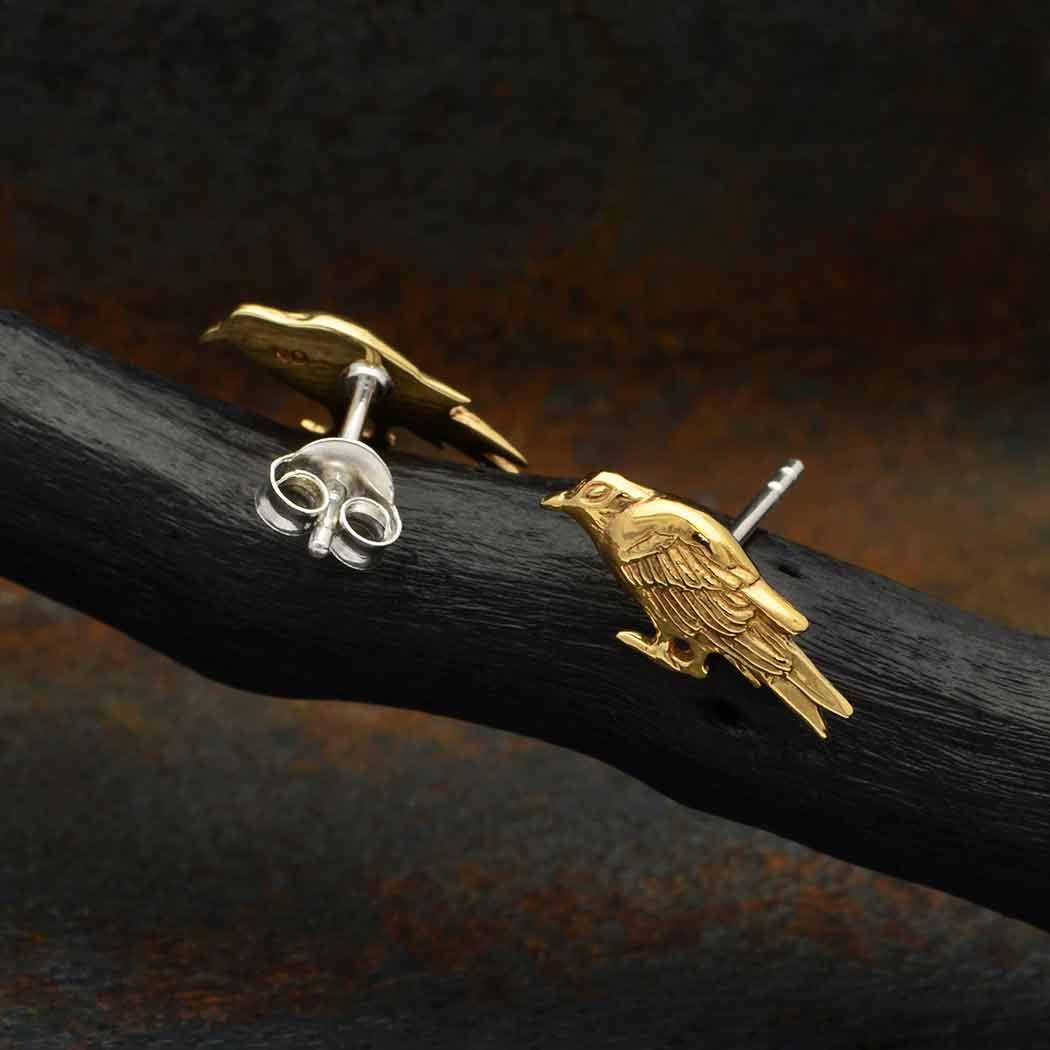 Bronze raven stud earrings with silver posts. Earrings are on a dark branch against a dark background