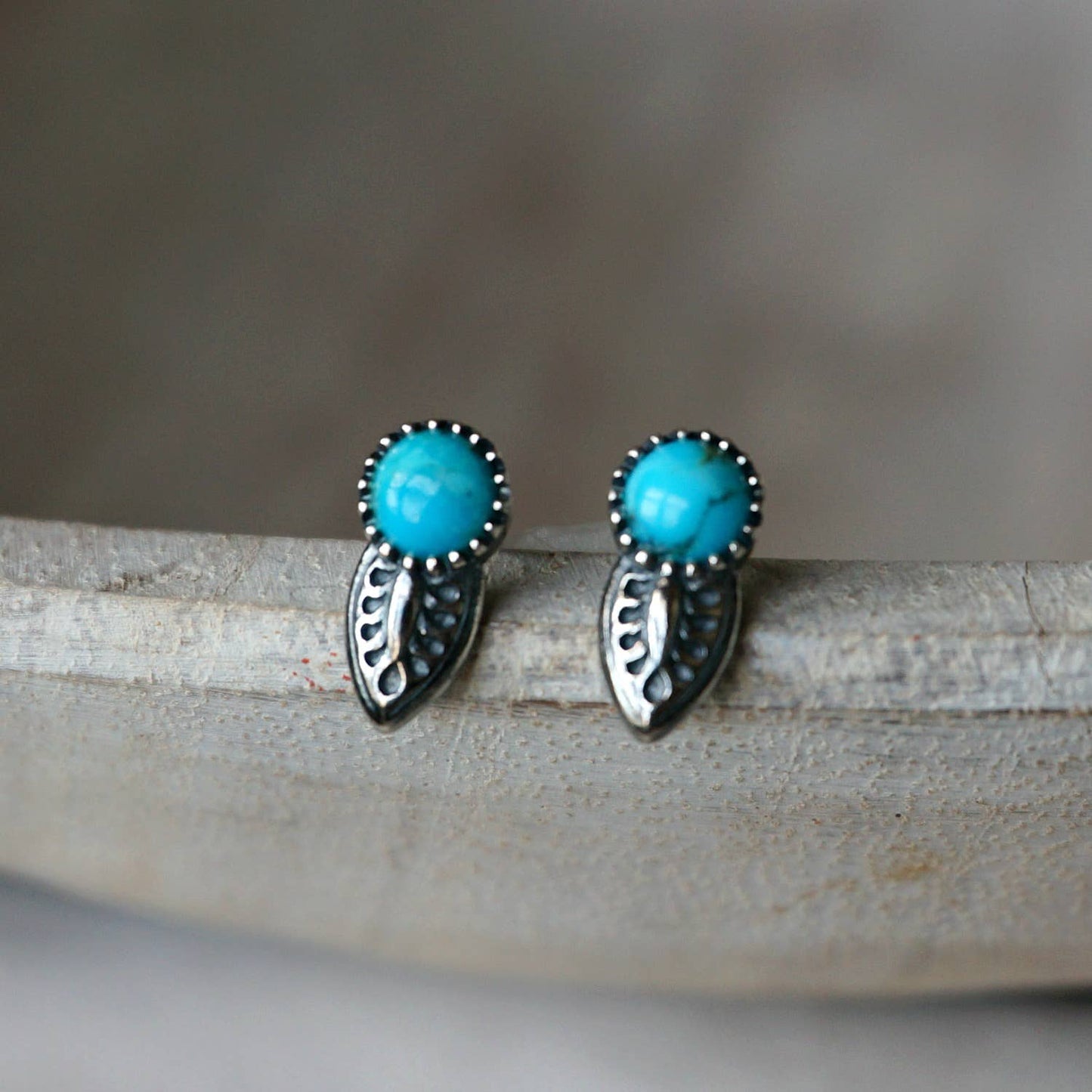 silver turquoise earrings with tooled leaf design on a grey background