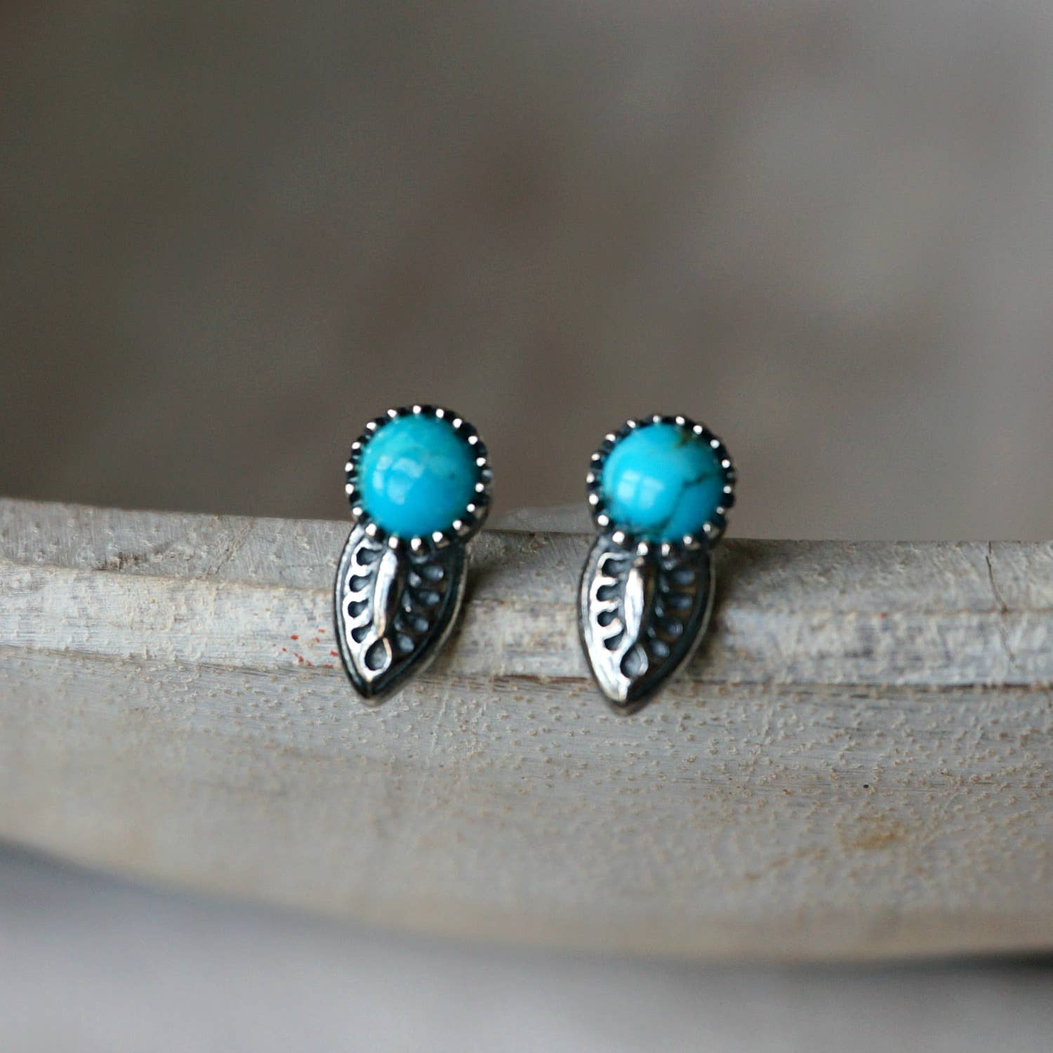 silver turquoise earrings with tooled leaf design on a grey background