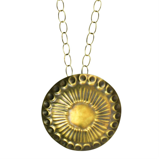 Pictured against a white background is a brass chained necklace with a circle shaped pendant that has circles on the border and lines throughout the center.