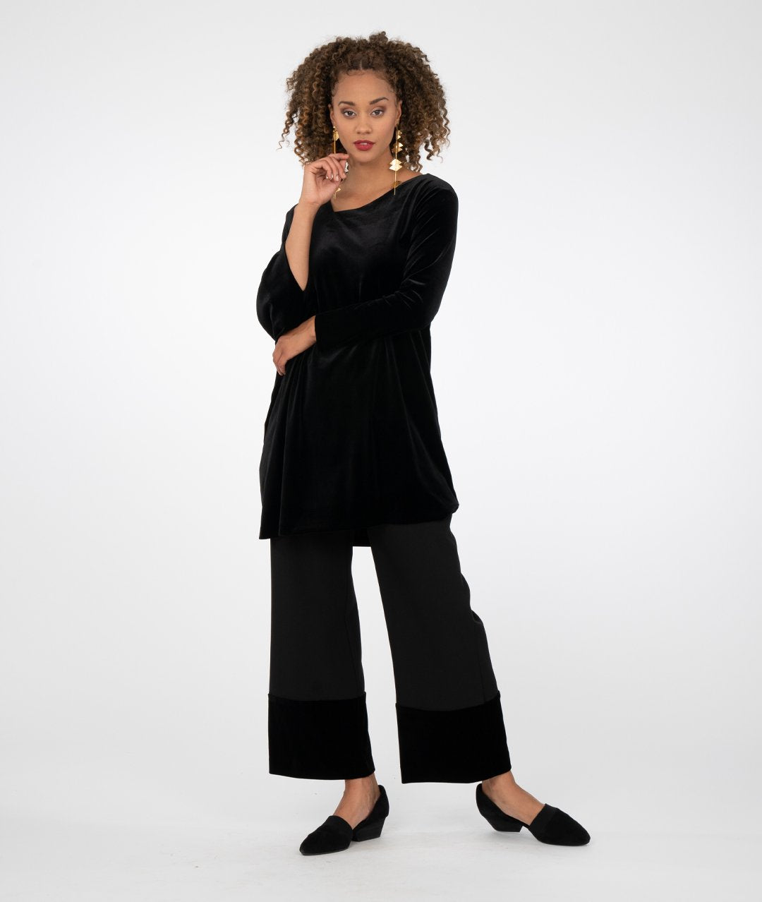 model in a black asymmetrical tunic worn with a wide leg black pant with a contrasting fabric at the bottom hems