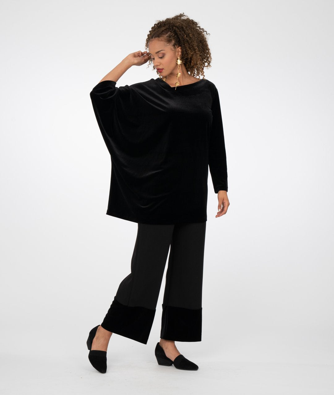 model in a black asymmetrical tunic worn with a wide leg black pant with a contrasting fabric at the bottom hems