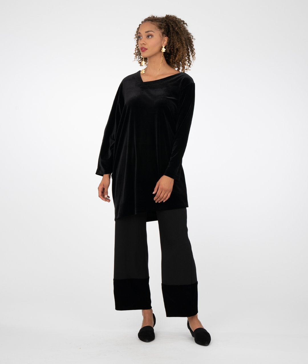 model in a black asymmetrical tunic worn with a wide leg black pant with a contrasting fabric at the bottom hems