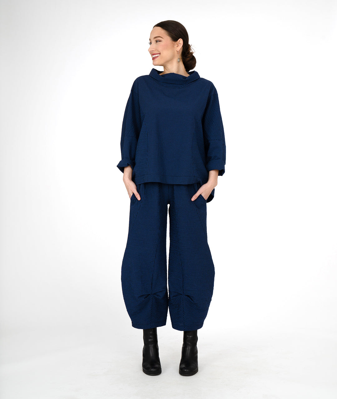 model in a boxy black and blue striped top with a cowl neck, worn with a wide leg pant in the same fabric with a tuck detail at either ankle