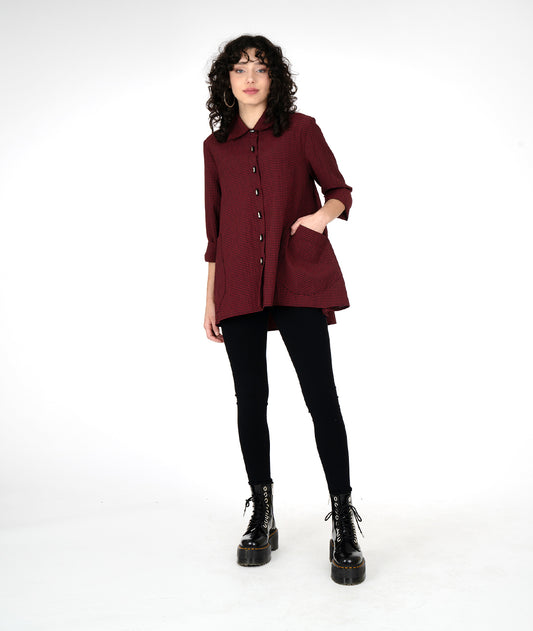 model in a long high-low button up blouse in a black and red stripe, with large rounded pockets on either hip, worn with black leggings and boots