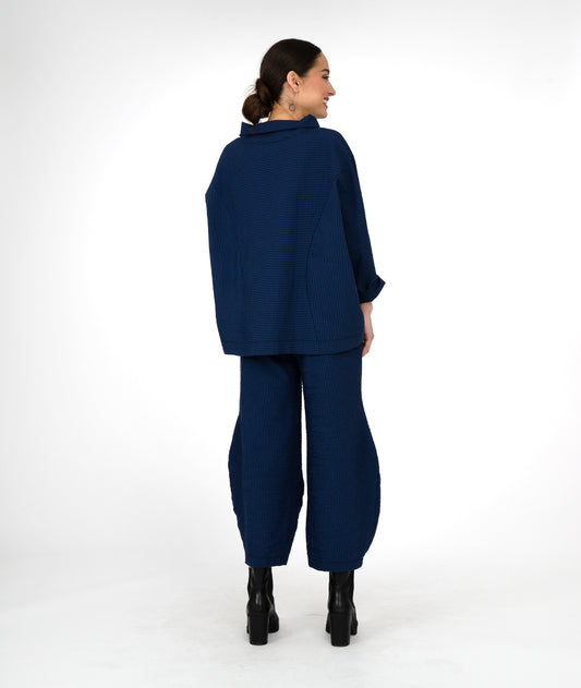 model in a boxy black and blue striped top with a cowl neck, worn with a wide leg pant in the same fabric with a tuck detail at either ankle
