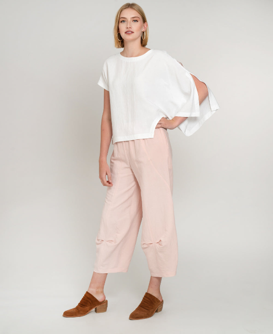 model in a blush pink pant with detailing at the hem, worn with an asymmetrical white top