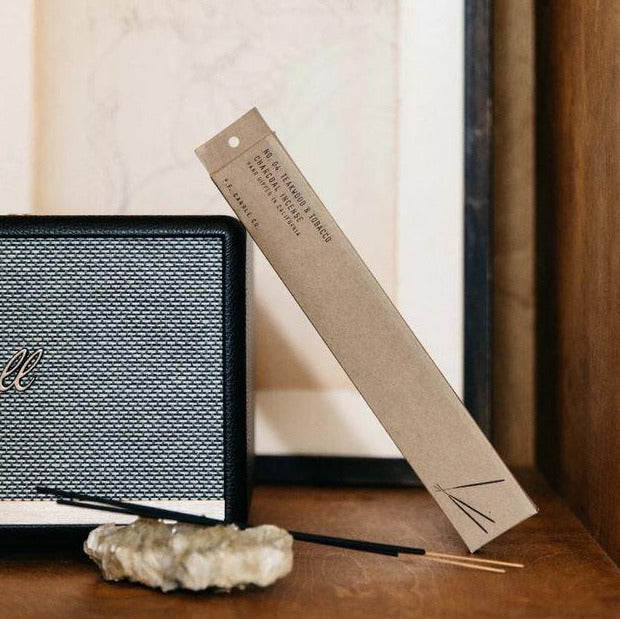 Featuring 2 sticks of black stick incense and their box, a narrow brown box that is labeled "teakwood & tobacco".