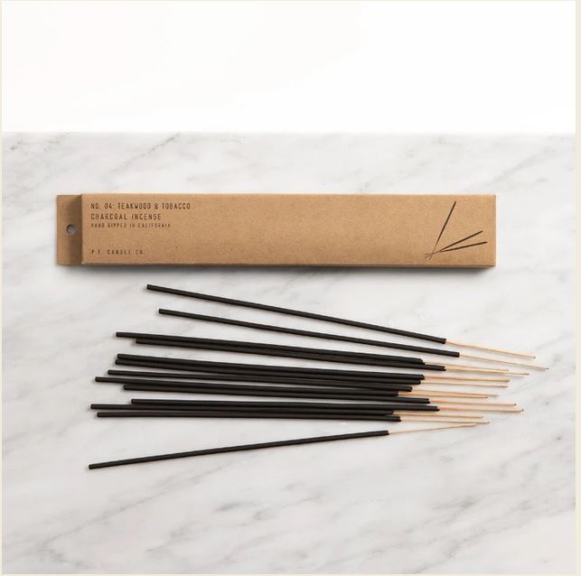 12 sticks of teakwood & tobacco scented incense are featured on a table, along with their packaging, a brown kraft paper box.
