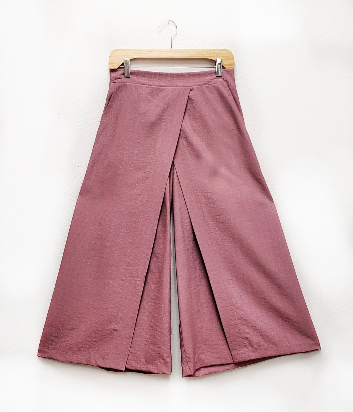 close up of mauve pant with flat front and skirt-like panels in the front. on a wooden hanger on a white background.