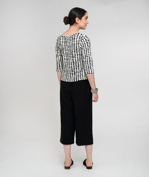 Pictured against a white background is the back view of a light-skinned model with black hair. She is wearing a 3/4 length sleeved black and white dot jersey top and black midi-length pants.