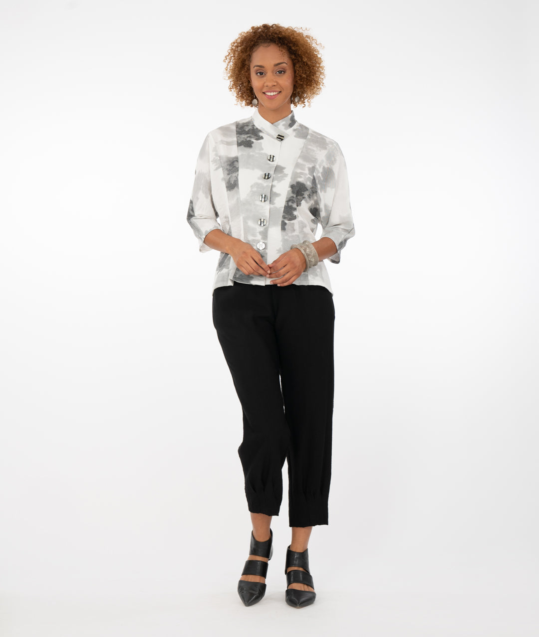 model in a white button up top with black and gray print, with black pants in front of a white background