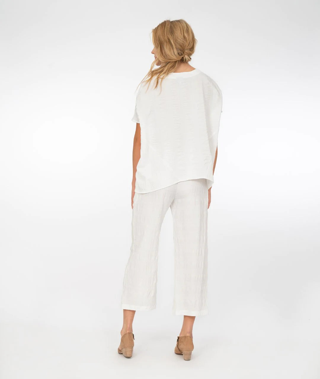 a model wearing white pants and a white boxy v-neck top in front of a white background