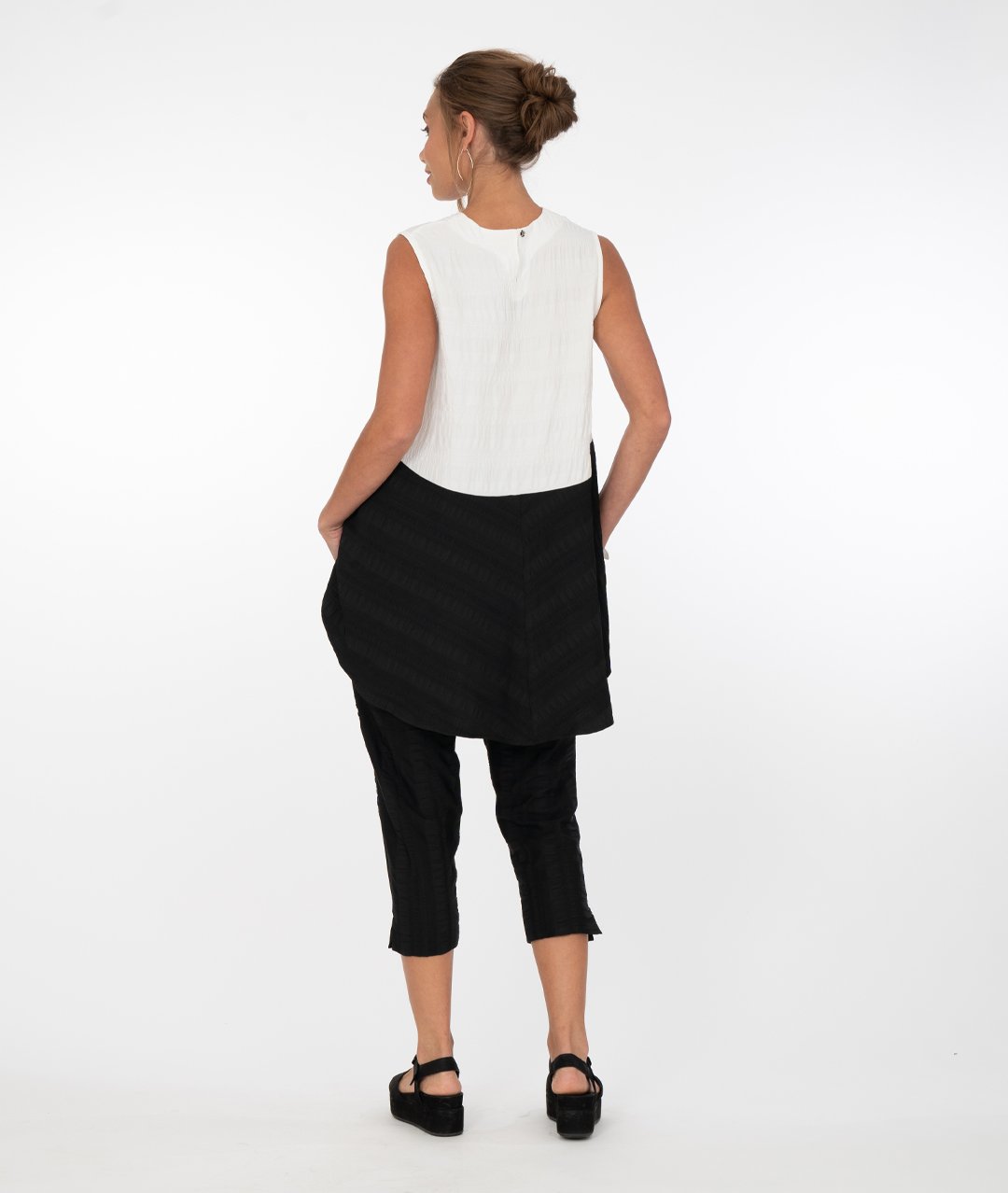 a brunette model wearing black capri pants with a black and white tank top in front of a white background