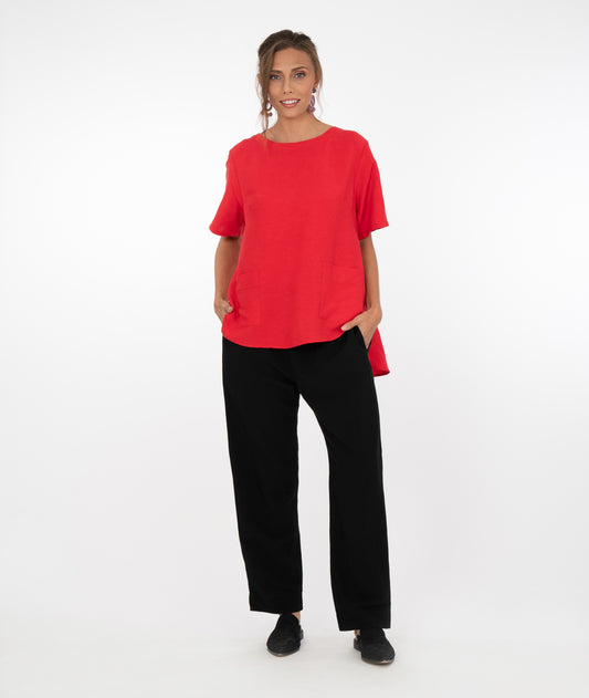 brunette model in a red top with black pants in front of a white background
