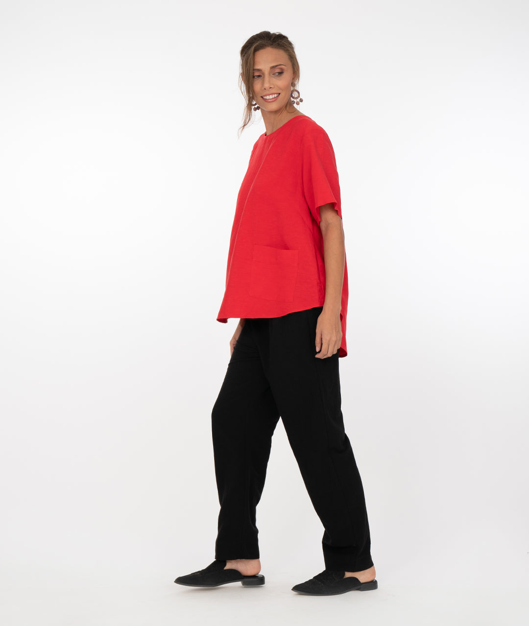 brunette model in a red top with black pants in front of a white background