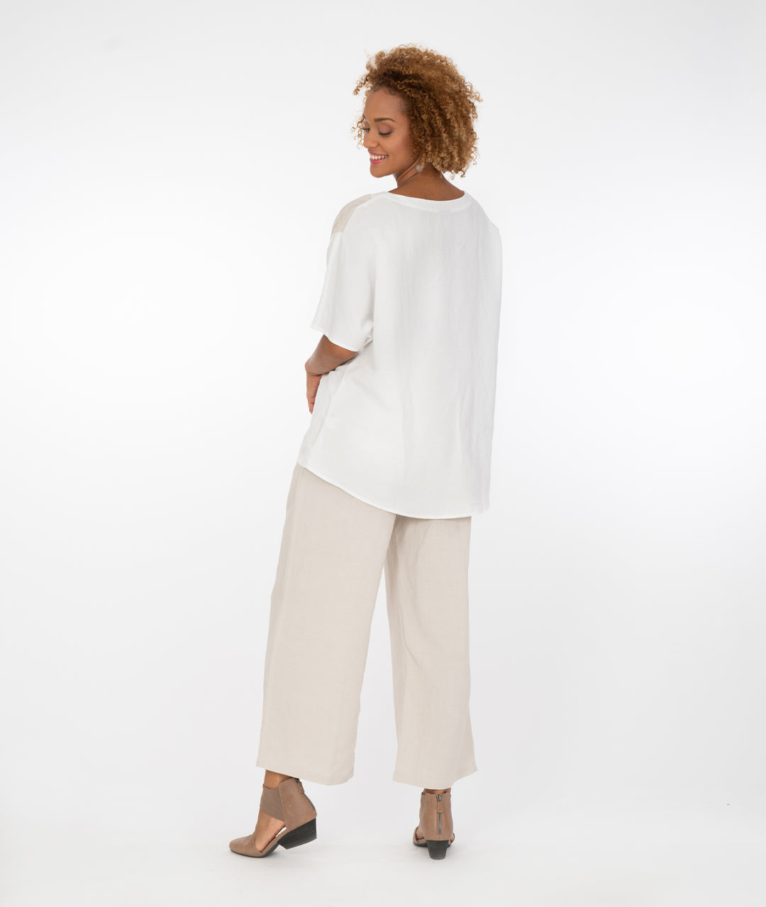 model in a white pullover tshirt style top with a contrasting color block across the body in a khaki color, with wide leg khaki color pants, back view