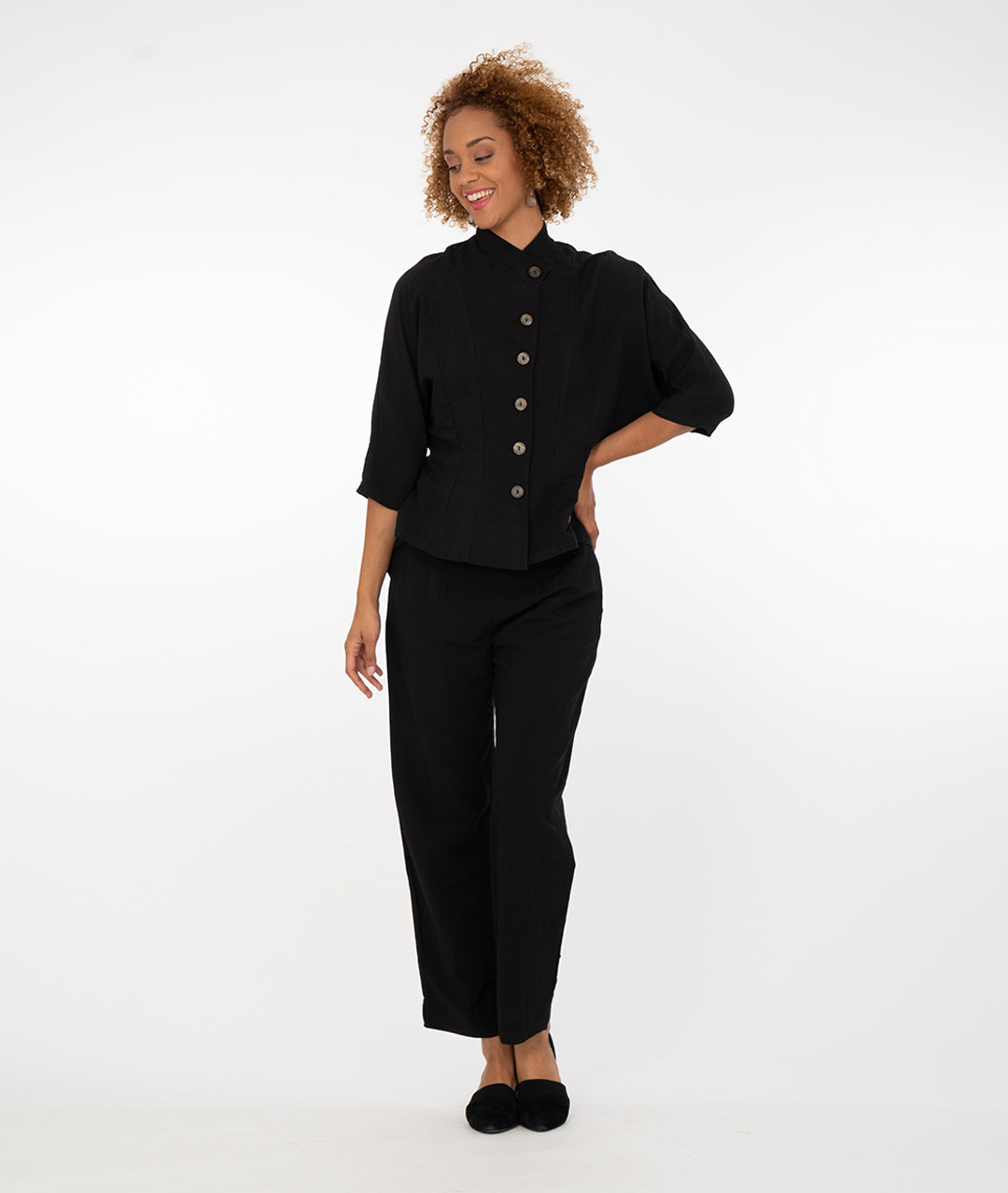 model in black pants with a black button up fitted black bouse with a dolman style sleeve and a short, asymmetrical standing collar