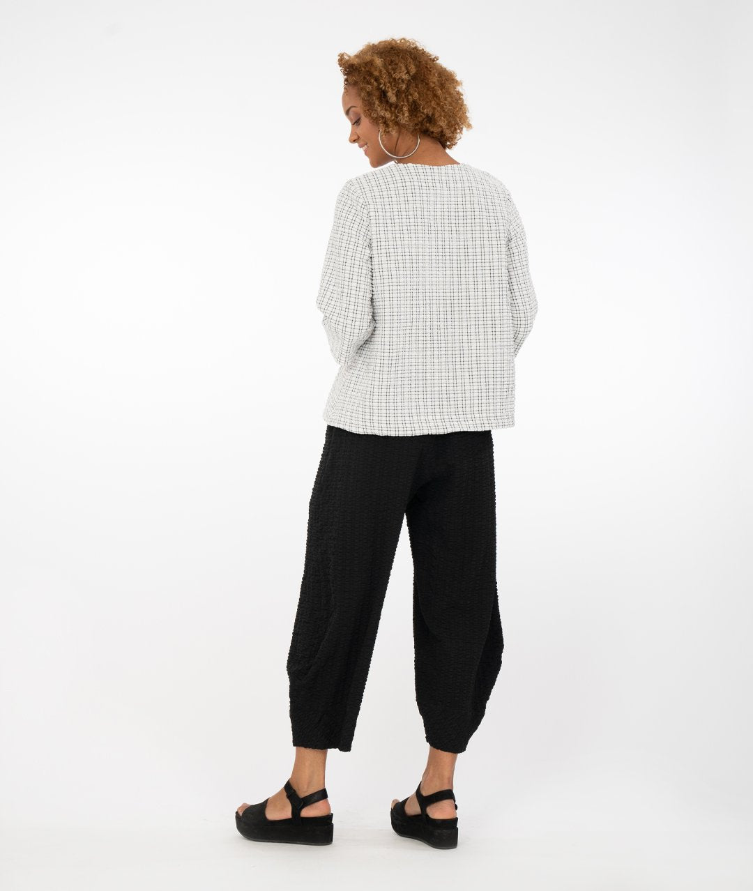 model wearing a black and white checked top with buttons at the front triangular overlap with black pants in front of a white background