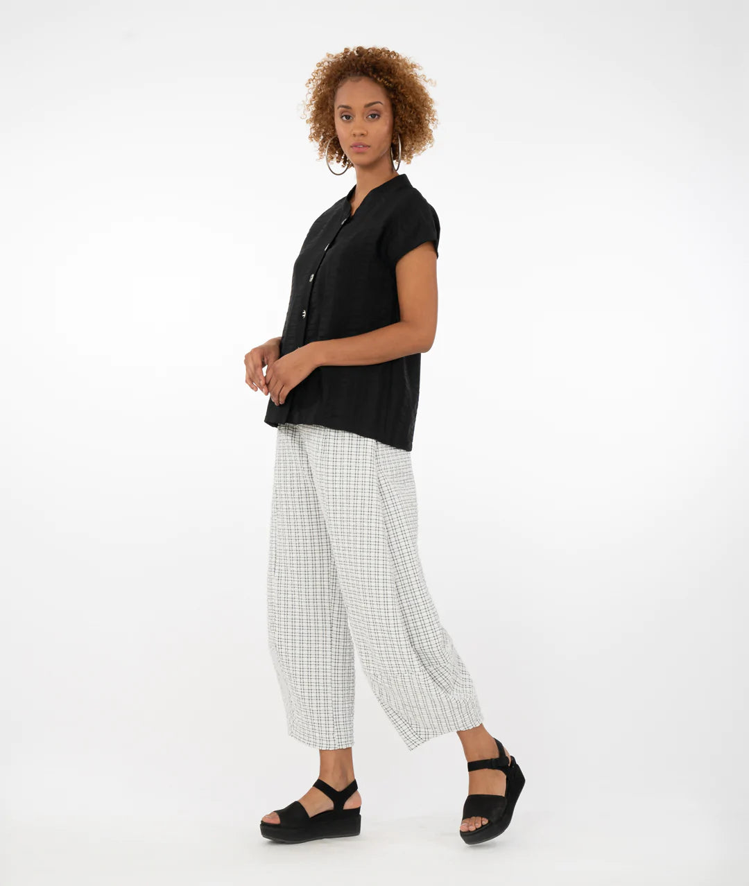 model wearing a black button up top with a black/white checkered pant in front of a white background