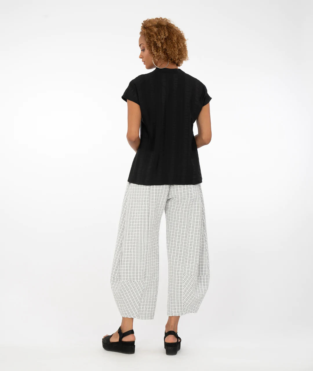 model wearing a black button up top with a black/white checkered pant in front of a white background