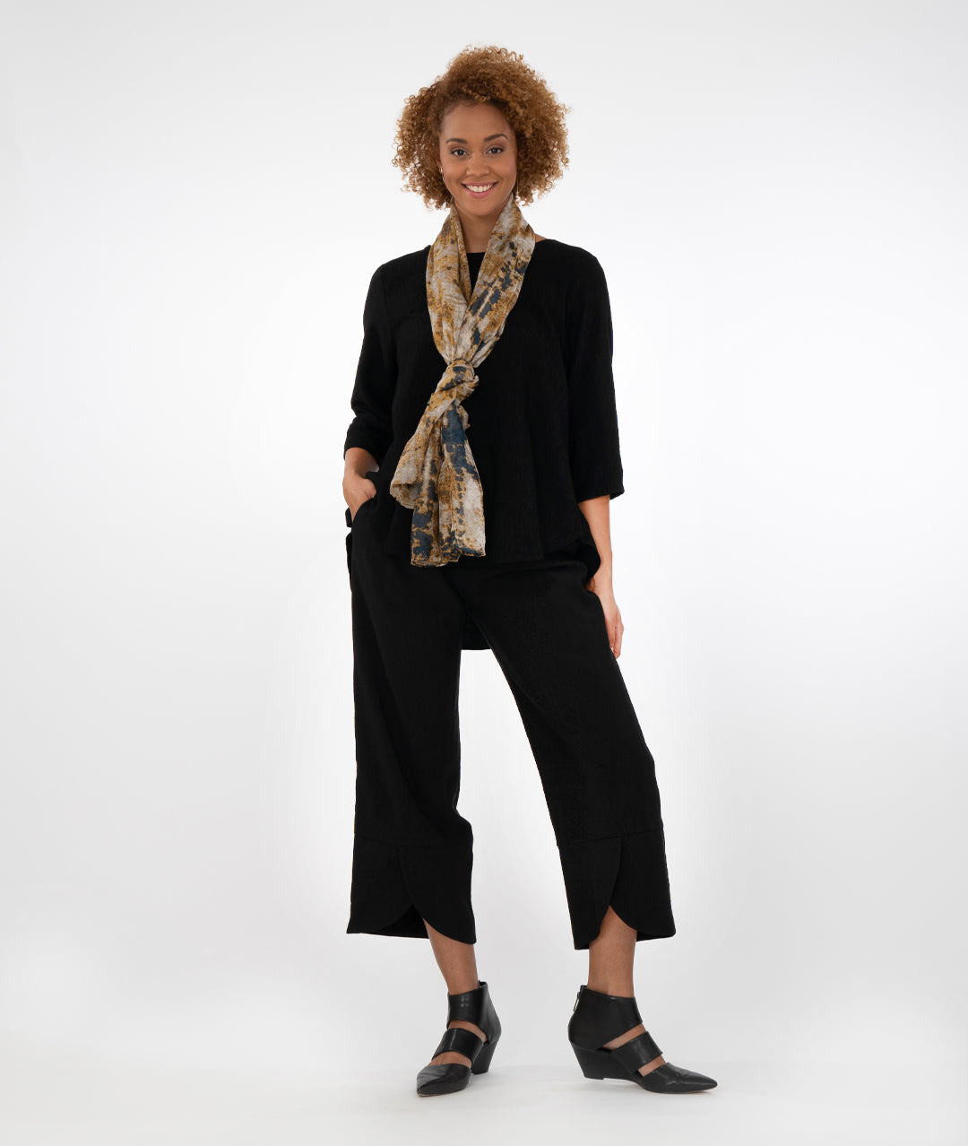 model in a black pant with a matching black top with a lower hem in the back and a scarf