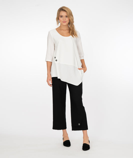 blonde model wearing a white top with black pants both with button detail in front of a white background