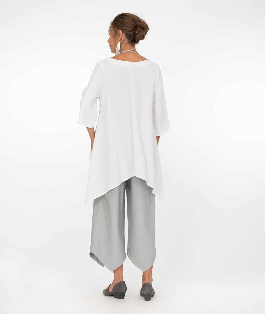 model in a grey pant with a pointed hem, worn with a white tunic with a long back