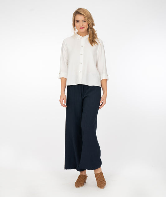 blonde model wearing a white button up shirt with navy blue pants in front of a white background