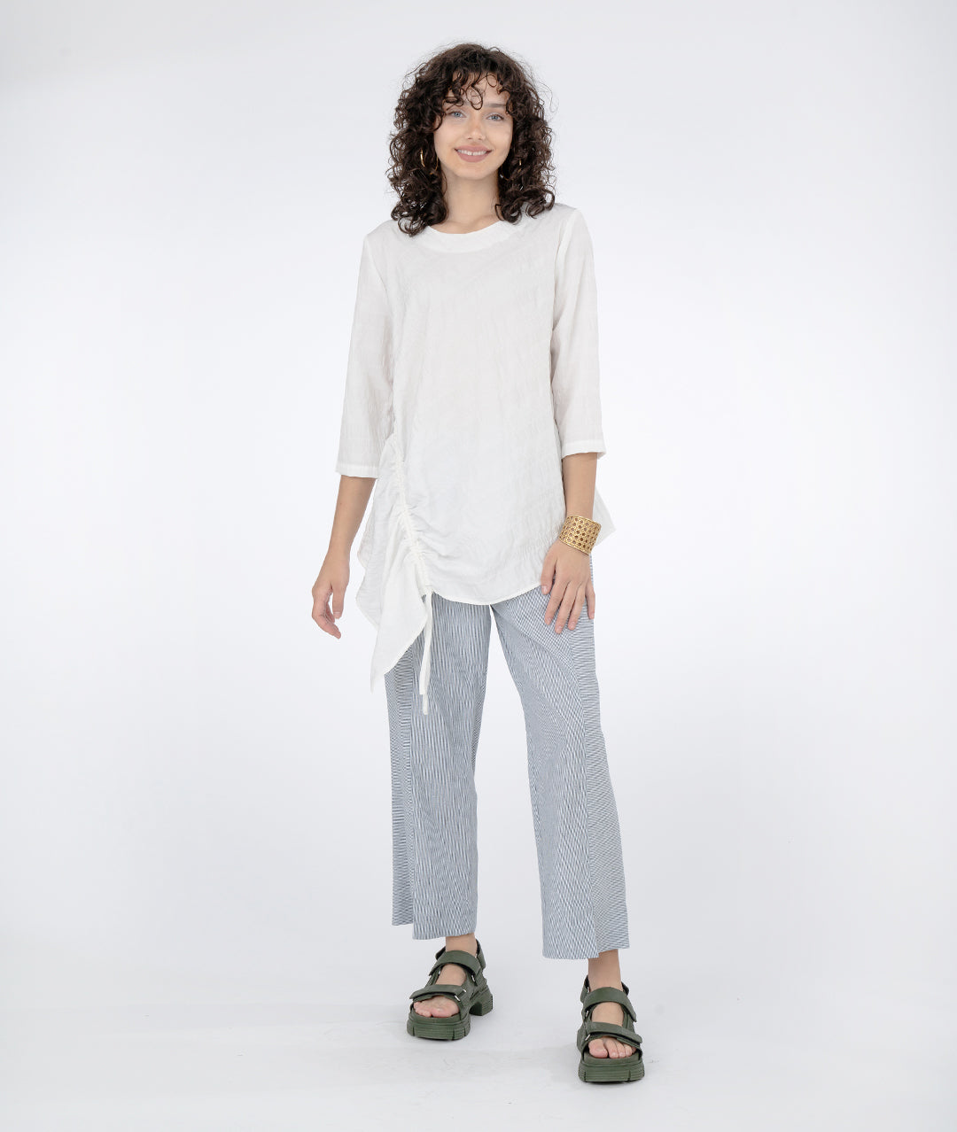model in a bule and white pinstriped pant with an asymmetrical white top with a gathered detail on the longer side and 3/4 sleeves