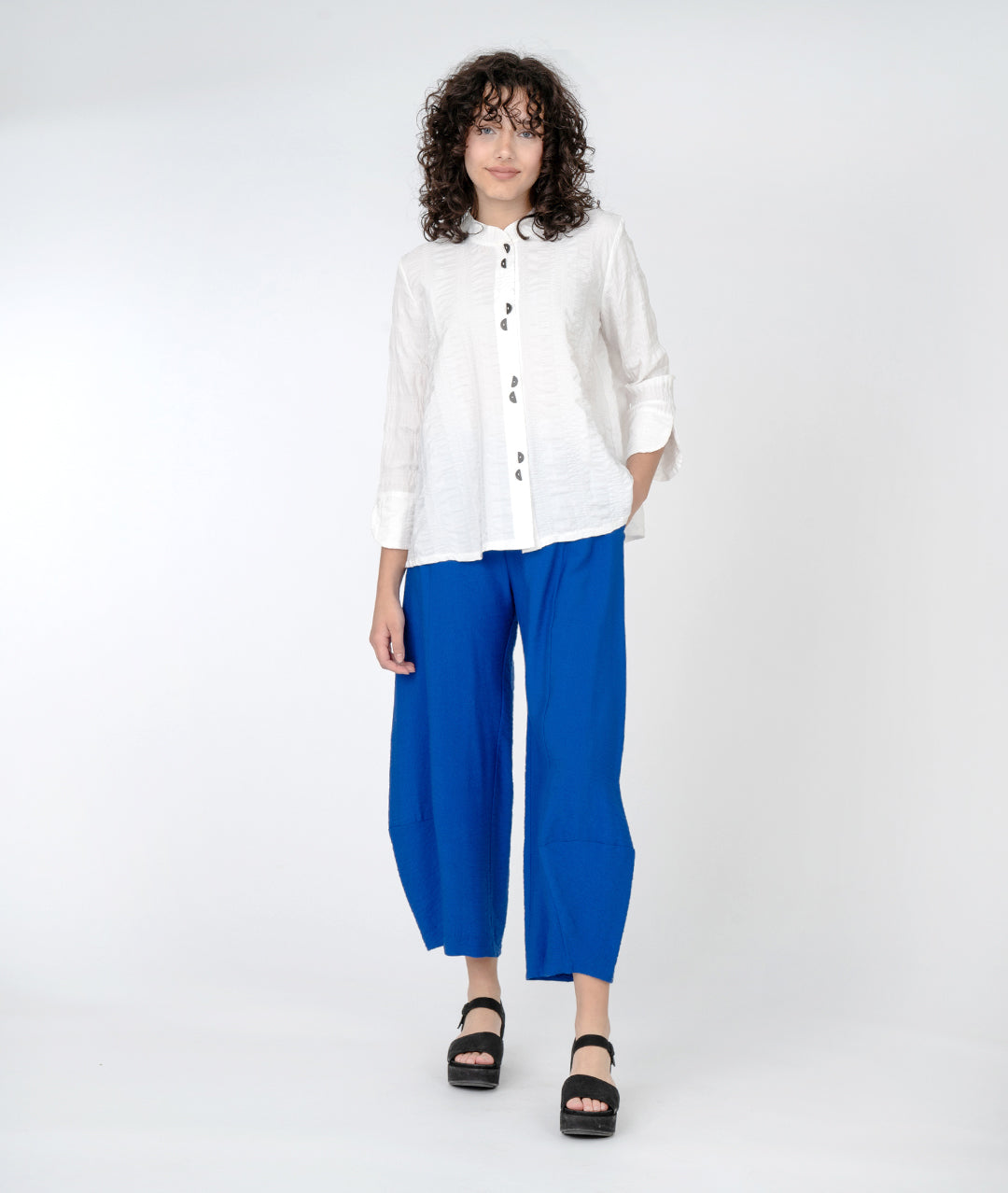 model in an electric blue pant with a swingy white button down blouse with 3/4 sleeves, a mandarin collar and half moon buttons